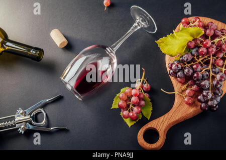 Ein Glas Wein mit einer Flasche, Korkenzieher und Trauben auf schwarzem Hintergrund Stockfoto