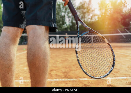 Der Mann hält Schläger beim Warten auf die Kugel in einen Tennisplatz. Der Mensch ist der Mittelpunkt und Vordergrund, Tennis net ist auf Hintergrund und unscharf Stockfoto