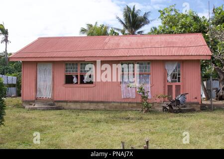 Ein rosa Haus mit einem Wellblechdach und einen Kinderwagen außerhalb, in einem Tongan Village auf der Insel Atata, Königreich Tonga Stockfoto