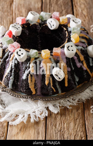 Hausgemachte Halloween Schokolade Bundt Kuchen mit kandierten Früchten, Eibisch und bunten Glasur close-up auf dem Tisch. Vertikale Stockfoto