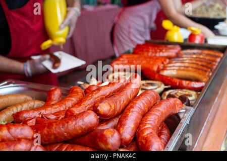 Ungekocht europäischen Würstchen. Gegrillte Würstchen und Leute im Hintergrund dienen. Stockfoto