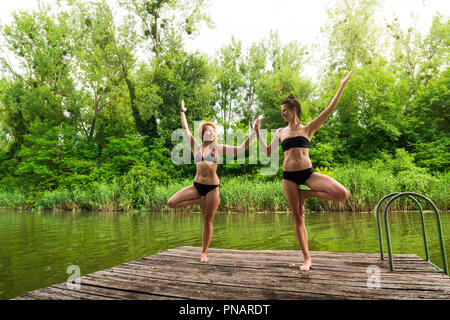 Freunde Üben Yoga auf dem Dock am See Stockfoto