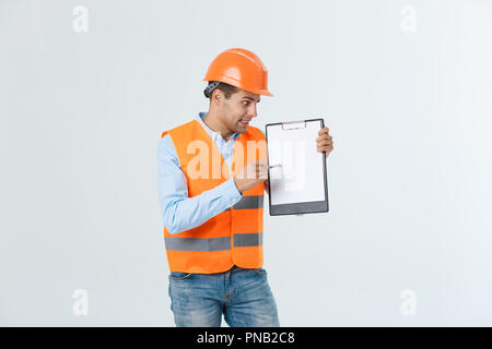 Frustrierte junge Ingenieur mit Schutzhelm und reflektierende Weste Prüfung auf Fehler im Dokument über grauer Hintergrund Stockfoto