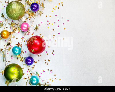 Bunte runde Weihnachtsbaum Spielzeug in verschiedenen Größen, twisted gold Garland, farbige Konfetti liegen auf einem weißen strukturelle Hintergrund horizontal wit Stockfoto