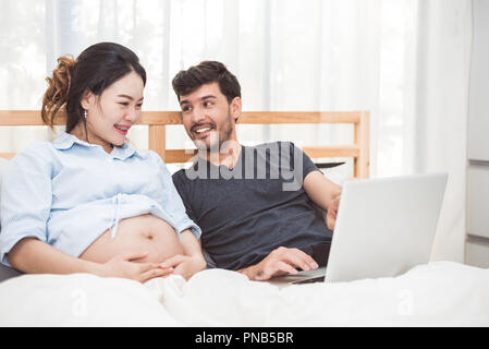 Glückliche Menschen und seine schwangere mit Laptop, um die Suche zu neugeborenen Baby Artikel für die Vorbereitung der Elternschaft Frau. Paar lifestyle Familie und Technologie Konzept. Stockfoto