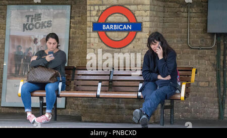 Zwei Frauen, die auf der Werkbank im Barbican Station, London Underground, England, Großbritannien warten Stockfoto
