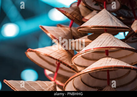 Orinetal, traditionelle Bambus und Stroh Hüte. Stapel von conic sun Hüte, rotem Futter und Blau, verschwommenen Hintergrund. Stockfoto