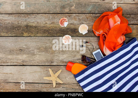 Sommer Kleidung und Accessoires: Handtaschen, Kopfhörer, Handy, Sonnenbrille, Sonnencreme auf alten Holz- Hintergrund. Stockfoto