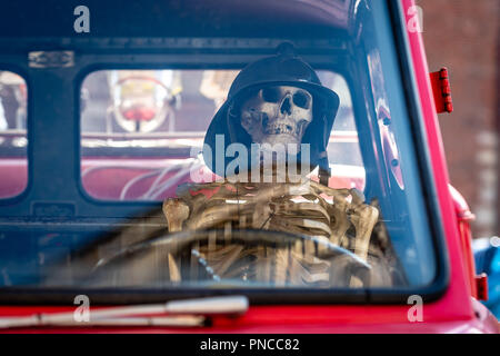 An der alten Feuerwehrauto, ein menschliches Skelett mit einem Feuerwehrmann, der Helm ist auf das Rad gelegt. Stockfoto