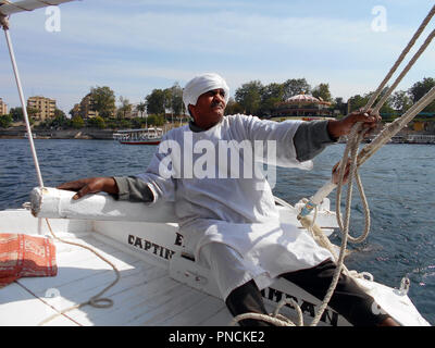 Ein ägyptischer Mann nimmt die Belastung an Bord seiner Feluke (kleines Segelboot), da er die Segel setzt auf dem Nil in Ägypten. Stockfoto