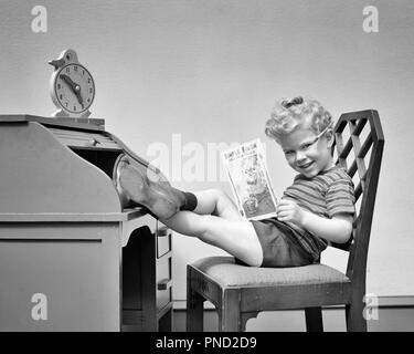 1940 s lockiges Haar blond Junge spielt Chef sitzen, FÜSSE AUF ROLLTOP SCHREIBTISCH UHR oben lesen Buch in die Kamera lächeln - j 9823 HAR 001 HARS JUVENILE CUTE FACIAL BLOND ENTSPANNENDE FREUDE FREUDE LIFESTYLE STUDIO SHOT HOME LIFE MANAGER KOPIEREN RAUM VOLLER LÄNGE MÄNNER FÜHRUNGSKRÄFTE AUSDRÜCKE B&W AUGENKONTAKT ERFOLG FRÖHLICHE CUSTOMER SERVICE LEADERSHIP ENTSPANNT, CURLY AUF BERUFE LÄCHELT BOSSE KONZEPTIONELLE FREUDIGE FÜSSE SCHERZEN JUGENDLICHE MANAGER ENTSPANNUNG SCHWARZ UND WEISS KAUKASISCHEN ETHNIE HAR 001 ALTMODISCH Stockfoto