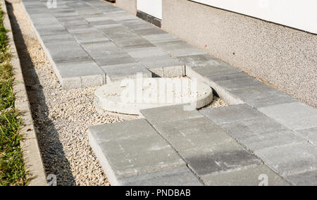 Festlegung grauer Beton Pflastersteine in Haus Hof Einfahrt, Terrasse. Installation neuer Fliesen und Platten um Abwasser- oder Kanal Abdeckung an der Auffahrt, Gehweg o Stockfoto