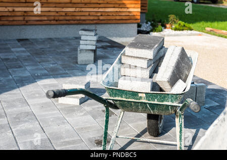 Festlegung grauer Beton Pflastersteine in Haus Hof Einfahrt, Terrasse. Schubkarren geladen mit neuen Fliesen oder Platten für Auffahrt, Gehweg oder Terrasse auf Le Stockfoto