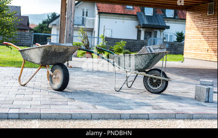 Festlegung grauer Beton Pflastersteine in Haus Hof Einfahrt, Terrasse. Schubkarren geladen mit neuen Fliesen oder Platten für Auffahrt, Gehweg oder Terrasse auf Le Stockfoto