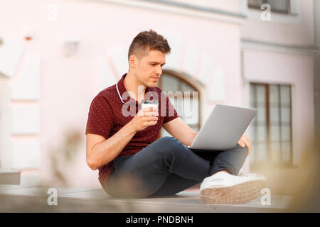 Junge Unternehmer blogger Mann trinkt Kaffee und arbeitet auf einem Laptop in der Stadt Stockfoto
