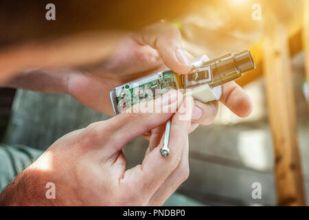Mann die Hände zur Festsetzung moderne Vaporizer e-cig Gadget vape e-liquid. Wartung elektronischer Geräte mech Mod vaping Gerät. Vaper Gerät reparieren Servi Stockfoto