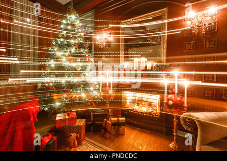 Geschenke an den Weihnachtsbaum. Weihnachten am Abend bei Kerzenschein. Classic Apartments mit einem Kamin. Stockfoto