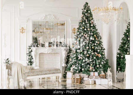 Geschenke an den Weihnachtsbaum. Weihnachten Morgen. klassische luxuriöse Apartments mit einer weißen Kamin, Sofa, großen Fenstern und Kronleuchter. Stockfoto