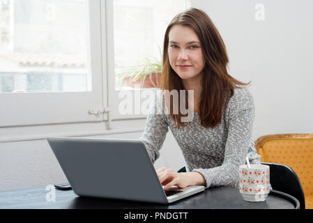 Schöne junge Frau mit Laptop an Kamera suchen Stockfoto