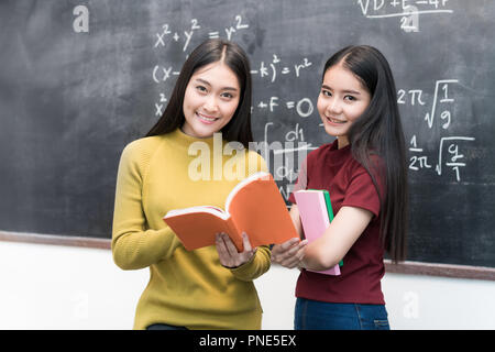 Asiatische Studentin über Tafel halten und lesen Bücher Togetherin Unterricht an der Universität. Bildungskonzept. Stockfoto