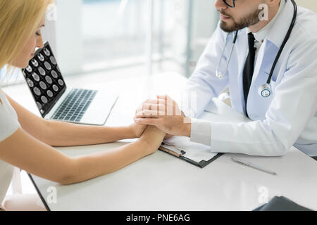 Freundliche mann Arzt Hände halten patient Hand am Schreibtisch für Ermutigung sitzen, Einfühlungsvermögen, Jubel und Unterstützung während der ärztlichen Untersuchung. Schlechte neue Stockfoto