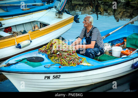 Alten Fischer seine Netze flicken in seinem kleinen Boot in den Hafen von Punat auf der kroatischen Insel Krk Stockfoto