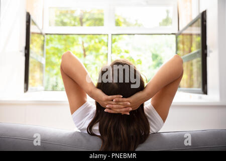 Rückansicht eines Frau sitzt auf einem Sofa vor dem Fenster Stockfoto