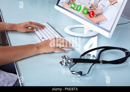 Doctor's Hand Video Conferencing auf Computer über Schreibtisch im Büro Stockfoto