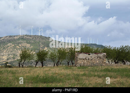 Eine spanische Aragonese Landschaft im Herbst mit einigen Windkraftanlagen über Berge, einige Orchard Bäume und eine verlassene Hütte aus Stein in einem Feld. Stockfoto