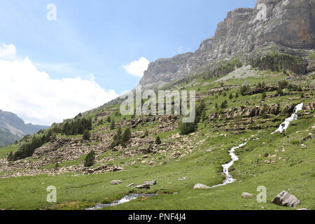 Eine Landschaft mit Wasserfall neben Arazas Fluss, in die hohen Berge und Gebirgsmassive, Kiefern und Tannen wald und tiefen blauen Himmel mit Wolken in Ordesa, Spanien Stockfoto