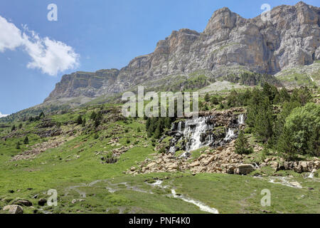 Eine Landschaft mit Wasserfall neben Arazas Fluss, in die hohen Berge und Gebirgsmassive, Kiefern und Tannen wald und tiefen blauen Himmel mit Wolken in Ordesa, Spanien Stockfoto