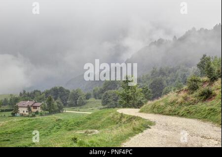 Eine Landschaft von eine Spur und ein einsames Haus in der montagnole Basse Bergen, in die Alpen, nach dem Regen und Nebel Wolken, nasses Gras und Bäume Stockfoto
