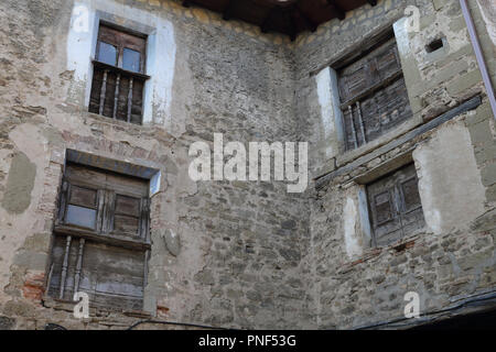 Vier kleine Fenster mit alten schäbigen Fensterläden aus Holz und einem Geländer auf einem Stein grau Häuser in Biel, einer kleinen Stadt in Aragon, Spanien Stockfoto