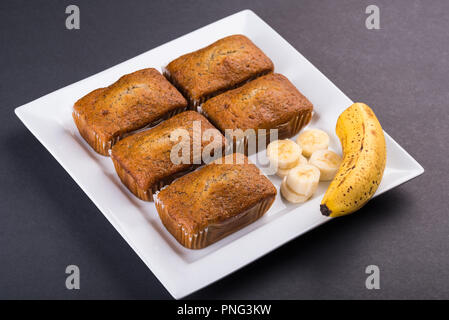 Frisch gebackene Banane Brote und Bananenscheiben auf einem weißen Teller und dunklen Tischplatte Stockfoto