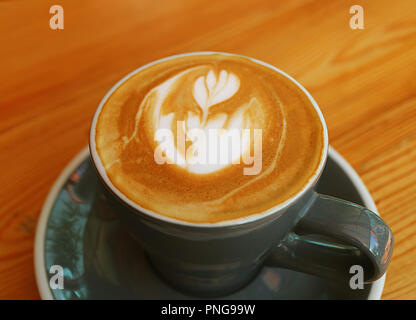 Geschlossen bis heißen Cappuccino mit Latte Art in einer dunklen grauen Schale serviert auf hölzernen Tisch Stockfoto
