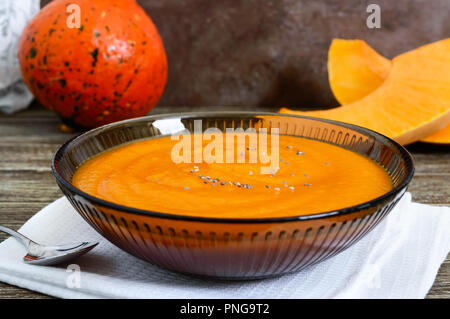 Zarte Kürbispüree in einem schwarzen Glas Schüssel auf einen hölzernen Tisch. Stockfoto