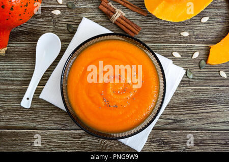 Zarte Kürbispüree in einem schwarzen Glas Schüssel auf einen hölzernen Tisch. Ansicht von oben. Stockfoto