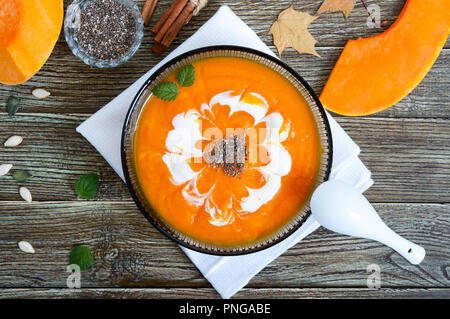 Zarte Kürbispüree mit Sahne und Chia Samen in ein schwarzes Glas Schüssel auf einen hölzernen Tisch. Ansicht von oben. Stockfoto