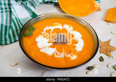 Zarte Kürbispüree mit Sahne und Chia Samen in ein schwarzes Glas Schüssel auf einem hellen Hintergrund. Stockfoto