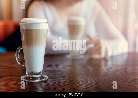 Latte Macchiato trinken im großen Glas hautnah. Kaffee sahne Cappuccino am Tisch im Café. Aufwachen, morgen sucht Konzept Stockfoto