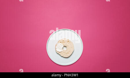 Die Hälfte Bagel auf eine weiße Platte mit Frischkäse auf einem rosa Hintergrund mit Platz für Kopie und Text angewendet Stockfoto