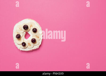 Die Hälfte Bagel mit Frischkäse, Blaubeeren, und in Scheiben geschnittenen Bananen auf einem rosa Hintergrund mit Platz für Text Stockfoto