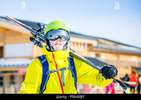 Bild von sportlichen Mann im Helm mit Skiern auf seiner Schulter gegen Gebäude Hintergrund Stockfoto