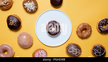 Classic Schokolade Ring Donuts mit Streuseln auf einem weißen Teller auf gelbem Hintergrund durch verschiedene andere eingerichtet Donuts mit Platz für Kopie umgeben. Stockfoto