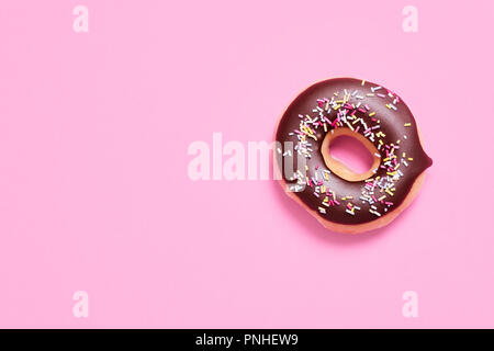 Klassische ring Donut mit Schokolade Zuckerguss und Streuseln auf einem Pastell rosa Hintergrund mit Platz für Text Stockfoto
