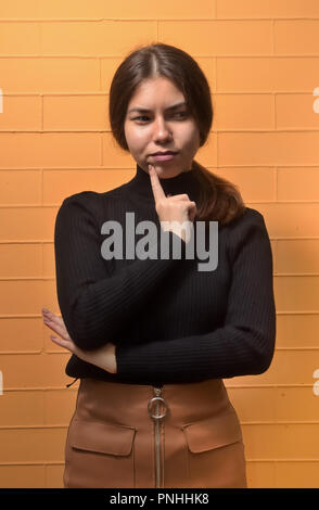 Porträt von einem asiatischen Mädchen, das denkt sich auf gelbem Backstein Hintergrund Stockfoto