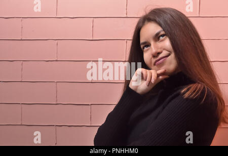 Nahaufnahme Porträt einer wunderschönen asiatischen Gesicht eines jungen Mädchen, das aussieht, halten sie ihre Hand in der Nähe von Kinn, das Bild horizontal, Crimson brick Hintergrund Stockfoto