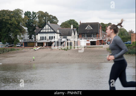 Weibliche Jogger laufen Vergangenheit Mortlake und Anglian Boat Club, London, Großbritannien. am gegenüberliegenden Ufer der Themse. Stockfoto