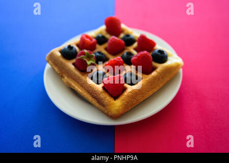 Belgische Waffeln mit Beeren auf blau und rosa Hintergrund Stockfoto