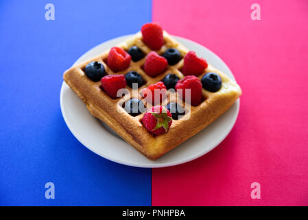 Belgische Waffeln mit Beeren auf blau und rosa Hintergrund Stockfoto